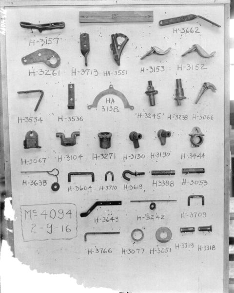 Parts displayed on a board with part numbers written next to each. At the top is a piece of paper that has a double-sided arrow with 12" written in the center. 