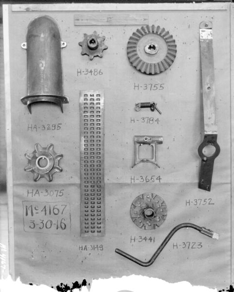 Parts displayed on a board with part numbers written next to each. At the top is a piece of paper that has a double-sided arrow with 12" written in the center.
