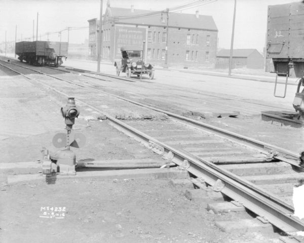 View across railroad tracks towards an automobile parked along a street. Commercial buildings are on the opposite side of the street.