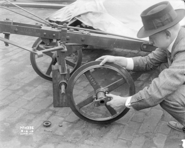 Close-up of a man wearing a suit and hat mounting a wheel onto a machine in the factory yard.