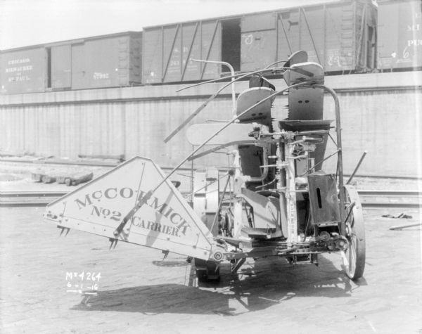 Corn Binder outdoors in the factory yard. A sign on the machine reads: "McCormick No. 2 Carrier." In the background are railroad cars on an elevated platform.