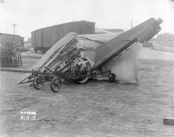 Corn Binder outdoors in factory yard. There is a cloth backdrop behind part of the binder. In the background are railroad cars.