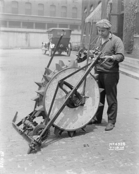 Man transporting piece of binder in factory yard at McCormick Works. In the background is an automobile parked near a brick building.