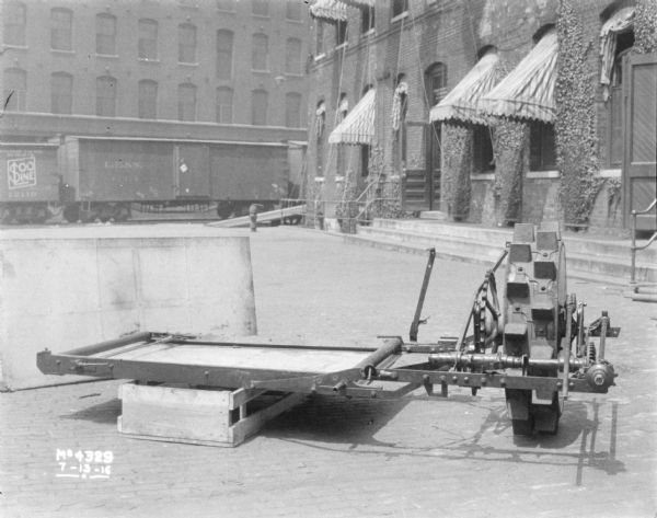 Assembly of Binder sitting in factory yard. Railroad cars and brick buildings are in the background.