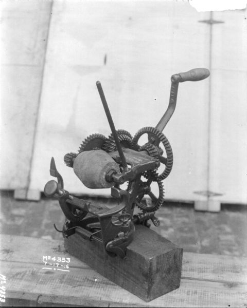 Hand-cranked blade sharpener attached to a block. It is set-up on a shelf outdoors in the factory yard with a backdrop behind it.