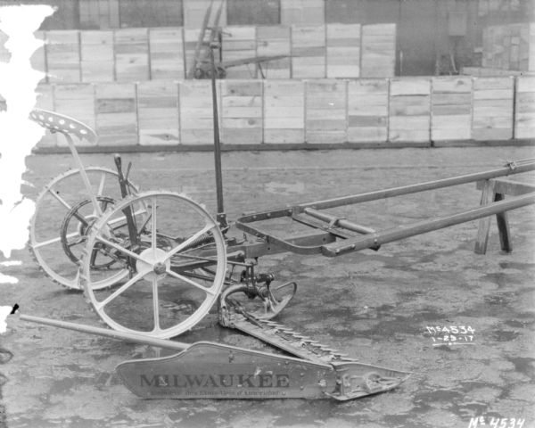 Mower at McCormick Works. A sign on the Mower blade reads "Milwaukee" with a sub-caption in French below. Crates, probably for shipping, are stacked near a brick building in the background.