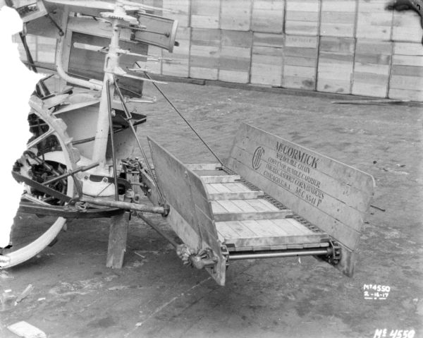 Corn binder outdoors in factory yard, with attachments, including a conveyor bundle carrier. Crates, probably for shipping, are stacked in the background.