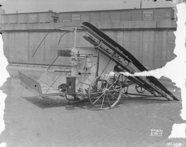 Corn Binder outdoors in factory yard. In the background are railroad cars on an elevated platform.
