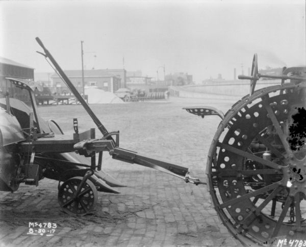 Detail of hitch between a tractor and a Corn Picker outdoors in factory yard. In the background are factory buildings and an elevated railroad platform.