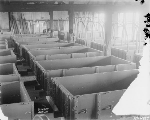 Slightly elevated view of wagon boxes lined up in rows inside a factory building.