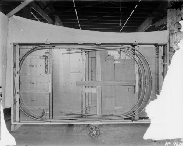 A wagon box has been turned on it side, showing the interior with metal support structure. White cloth backdrops are set up around the wagon, which is inside a factory.