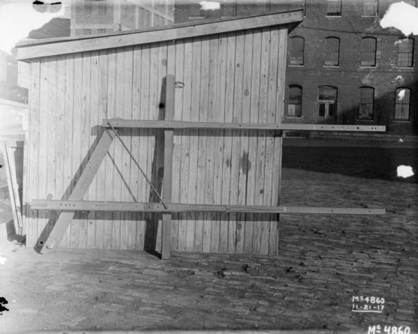 A hitch is set-up against the wall of a shed outdoors in the yard at McCormick Works. A brick factory building is in the background.