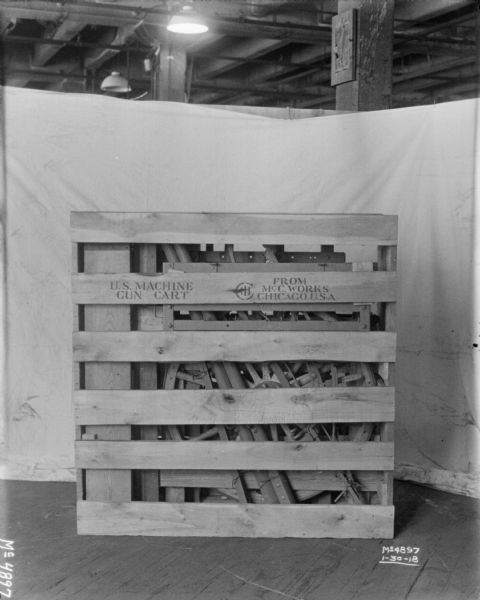 Gun cart crated for shipment on factory floor, labeled "US Machine Gun Cart." There is a backdrop behind the crate.