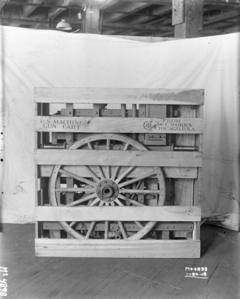 Gun cart crated for shipment on factory floor, labeled "US Machine Gun Cart." There is a backdrop behind the crate.