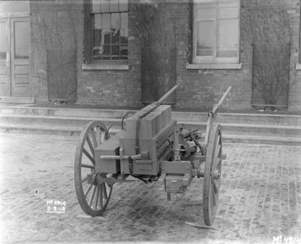 Gun Cart outdoors on cobblestones in factory yard in front of a brick building. The machine guns are mounted.