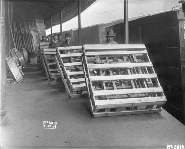 Line of employees with crated machines on a loading dock, loading them onto boxcars.