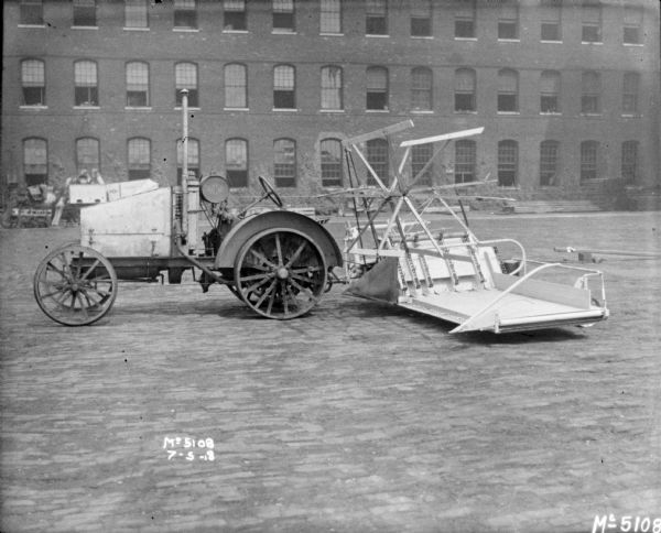 Tractor-Drawn Binder outdoors in factory yard. There is a brick building in the background. 