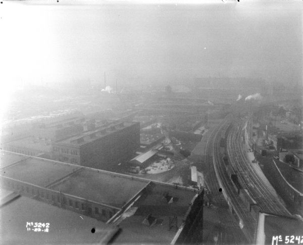 View of factory buildings, yard, and railroad tracks, including smokestacks.