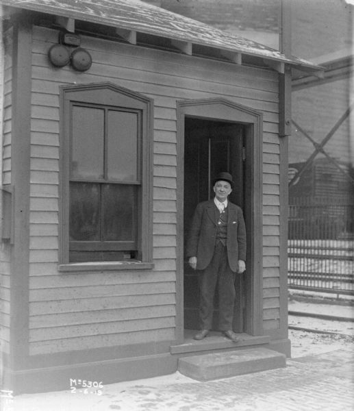 View towards a man standing in the doorway of a small building in factory yard.