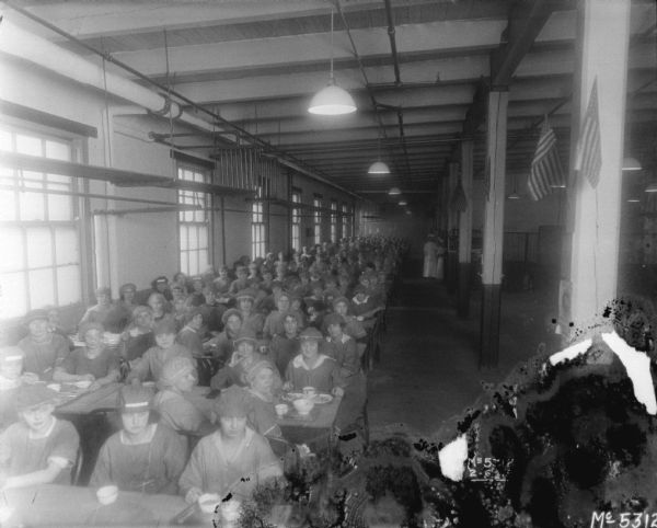 Slightly elevated view of women eating in the dining room. They are posing for the camera. Flags are hanging from the columns in the room.
