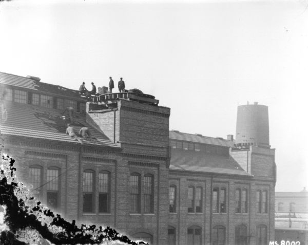 Men are working on constructing the roof of a large, brick building.