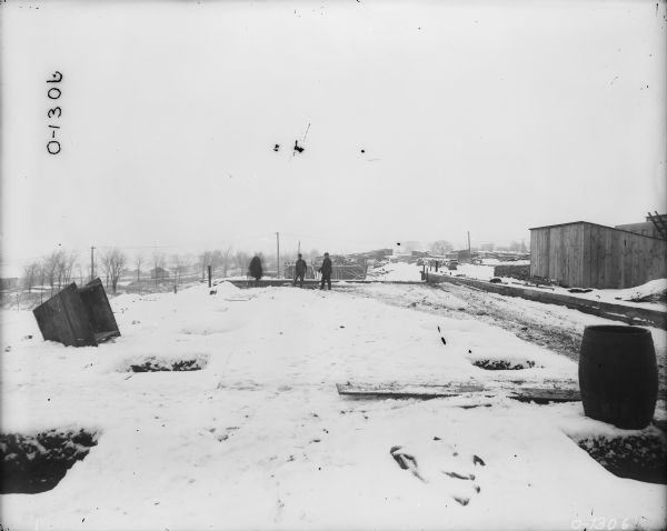 Men are standing in the snow near a plant under construction.