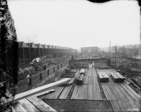 View from platform looking down towards men working on buildings under construction. Houses are on a hill in the distance.