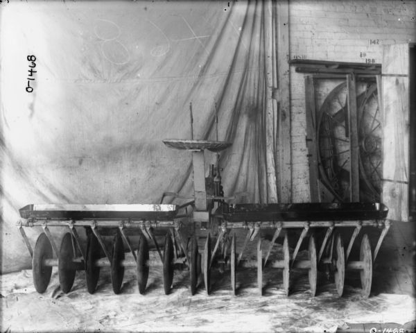 Agricultural part set up indoors on a cloth. There is also a cloth backdrop behind on the left. On the right is a brick factory wall.