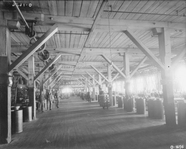 Men are standing inside what may be International Harvester's Osborne Works. Belt-driven machinery is attached to the ceiling.