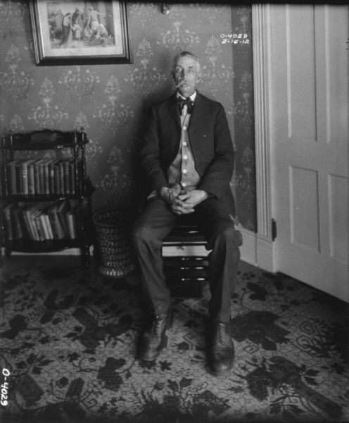 A man wearing a business suit is sitting in a chair in the foyer of a home.