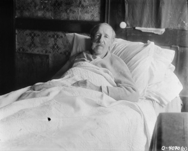 An elderly male employee is sitting up in bed.