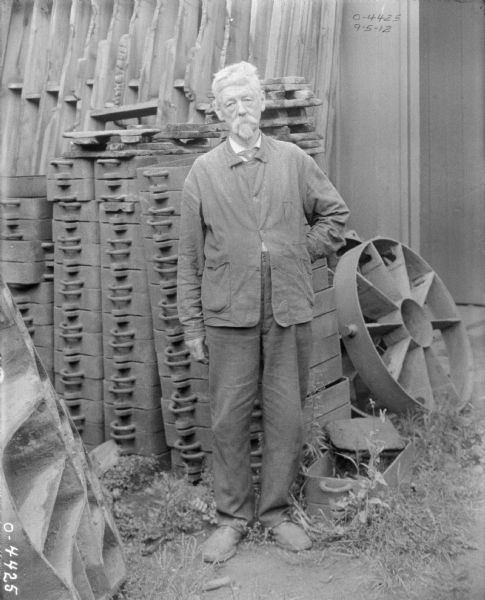 Elderly man standing and posing beside stacks of parts molds.