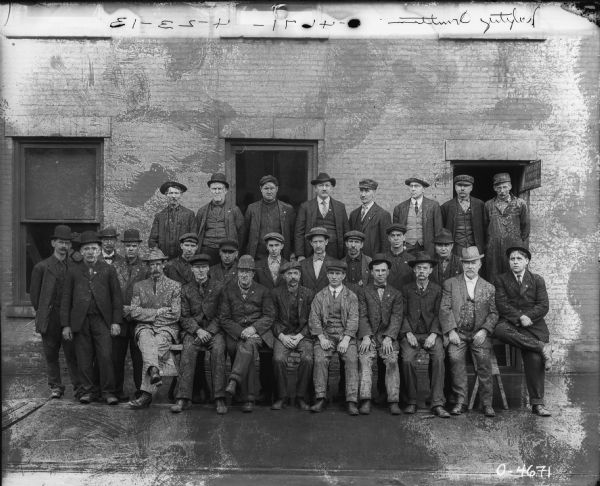 Outdoor group portrait of men standing in front of a brick building. "Safety Committee." A sign at the doorway reads: "Employment Office."