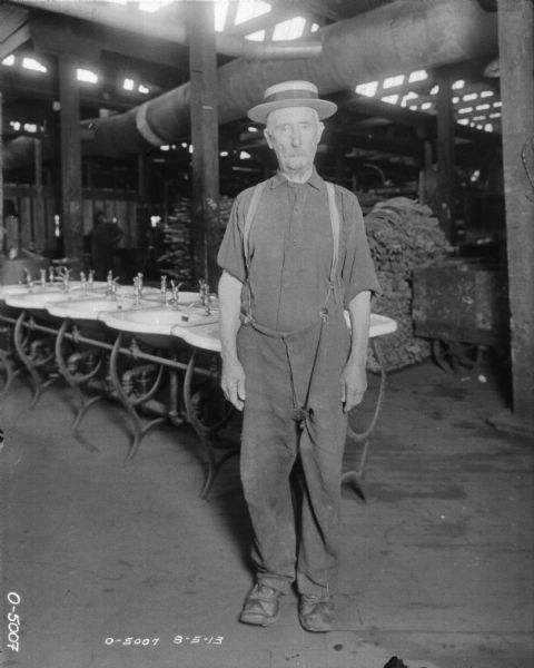 A man wearing a hat is standing in front of a long row of sinks, with a factory floor in the background.