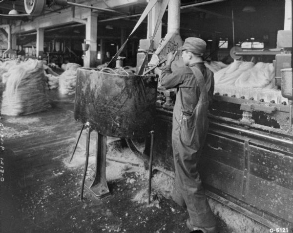 A man is working with a twine manufacturing machine on a factory floor. Bales of twine are in the background.