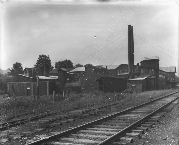 View across railroad tracks towards weathered and worn warehouse buildings near a plant.