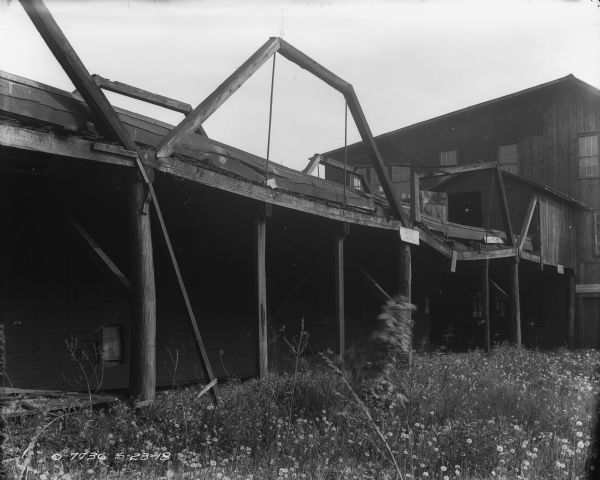 View across tall grass along a bridge or wall towards plant buildings. A sign reads: "Danger; Low bridge." Another sign above a door on the right reads: "No Admittance, Inquire at Office."