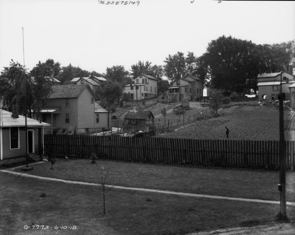 Slightly elevated view across yards and fences of a neighborhood on a hill. A man is standing in the yard in the center just beyond a fence.