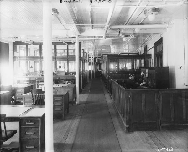 Interior view of a large office, with a female switchboard operator sitting on the right.