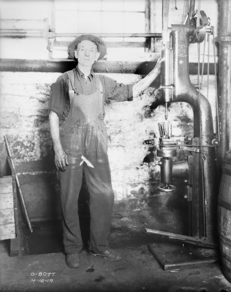 Full-length portrait of a man wearing overalls and a hat standing at a drill.