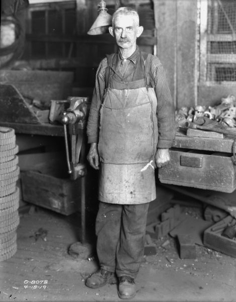 Indoor portrait of a man wearing a work apron, standing next to a lathe.