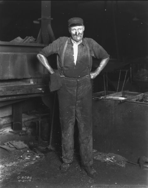 Full-length portrait of a man standing indoors with his hands on his hips at welders bench.