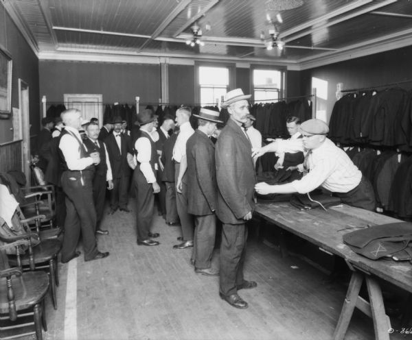 Employees being fitted with suits. Suits are hanging from racks in the background.