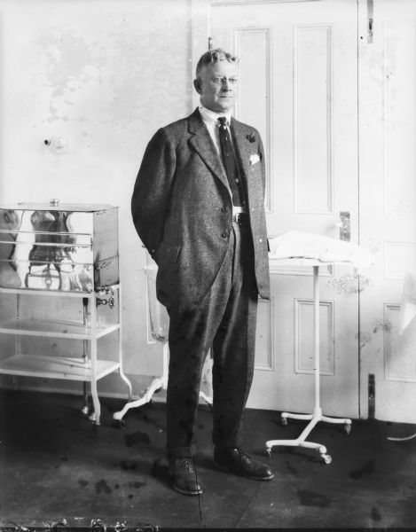 Full-length portrait of a man wearing a suit and standing in an infirmary.