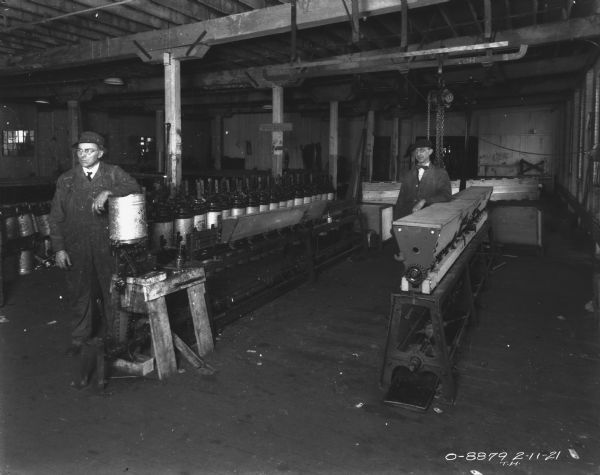 Construction sequence of Disk Harrows, with attachments and seeders. The two men are standing and wearing work clothes over their shirts and ties. Both men are also wearing eyeglasses and hats.