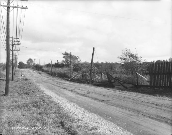Collapsed fence along roadside. Power poles are along the road on the left and right.