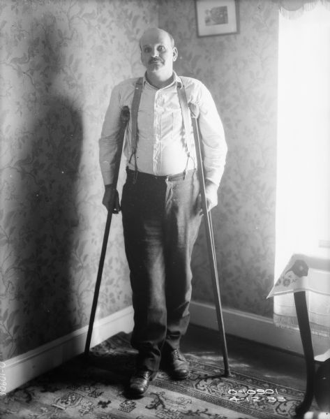 A man is standing indoors on crutches.