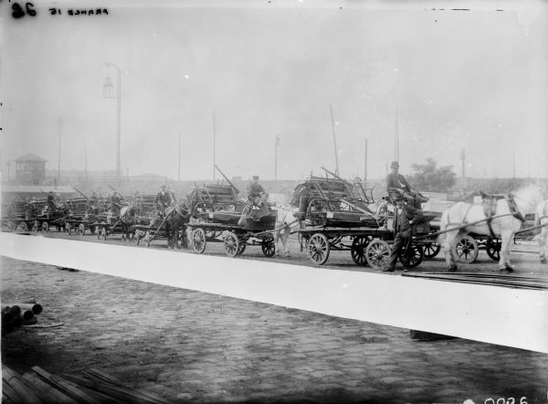 Line of binders being transported by mule cart. Men are posing on the carts. Wallut Dealership. Location: France.