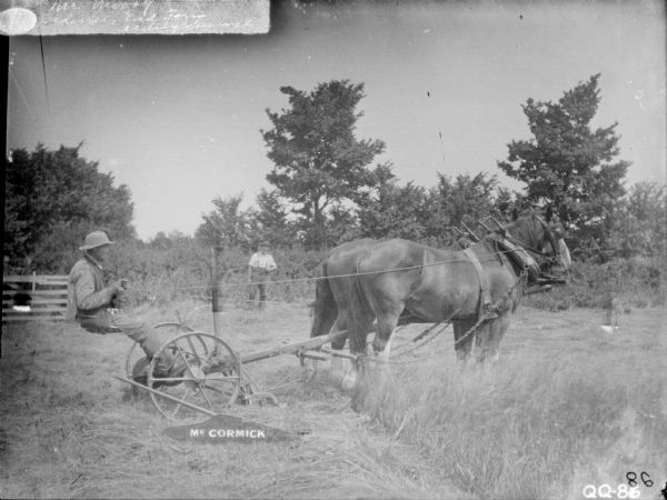 Right side view of a man using a McCormick mower pulled by a team of two horses. Another man is standing in the background. Labeled: "Mr. Moody, Gardener, End Farm, Ardely Skeverse"(?). Location: England.