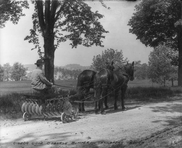Right side view of a man driving an Osborne Bumper Disk Harrow on a horse-drawn transport truck.